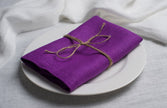 Violet linen napkin tied with jute twine on a white plate, side view