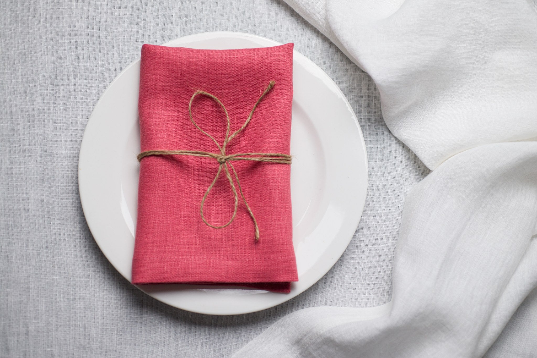 Salmon linen napkin tied with jute twine on a white plate