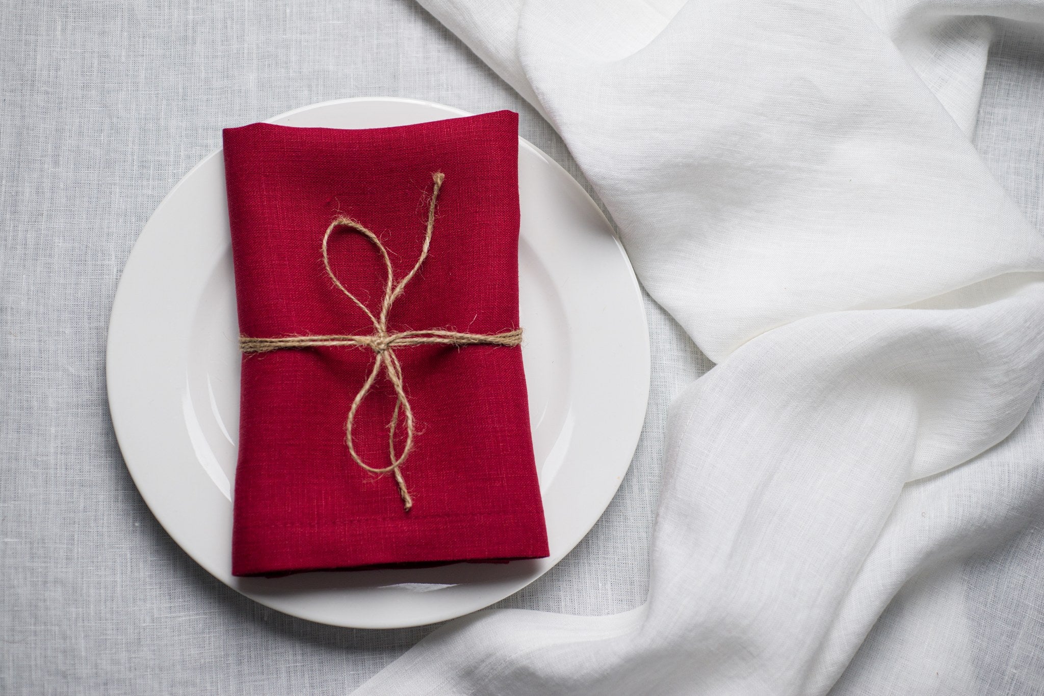 Wine linen napkin tied with jute twine on a white plate