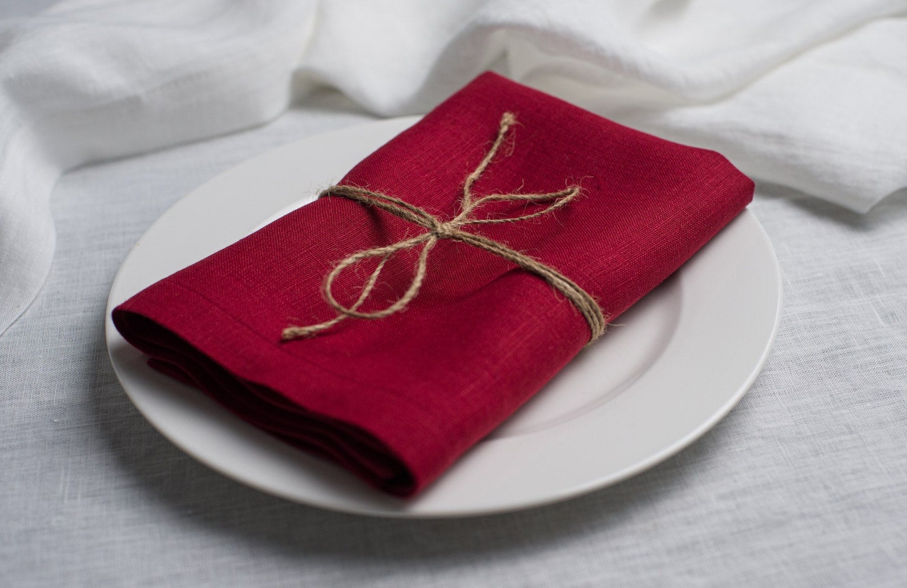 Wine linen napkin tied with jute twine on a white plate, side view