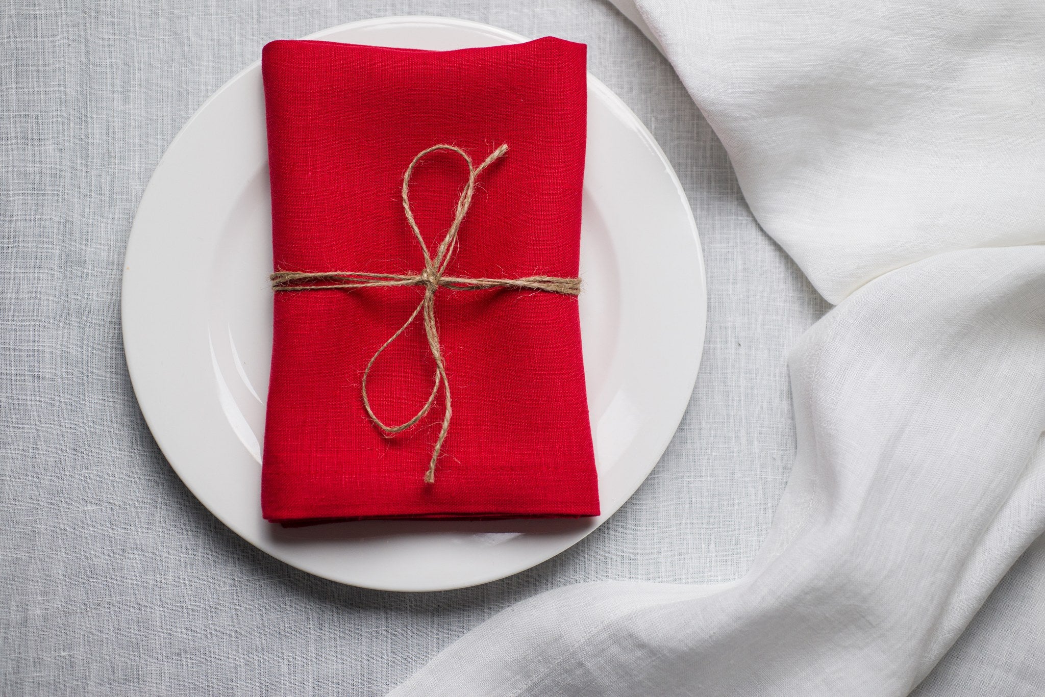 Red linen napkin tied with jute twine on a white plate