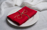 Red linen napkin tied with jute twine on a white plate, side view