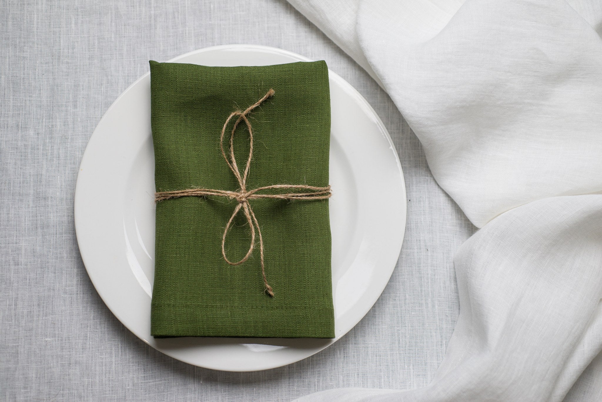 Green linen napkin tied with jute twine on a white plate