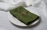 Green linen napkin tied with jute twine on a white plate, side view