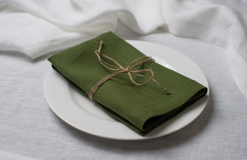 Green linen napkin tied with jute twine on a white plate, side view