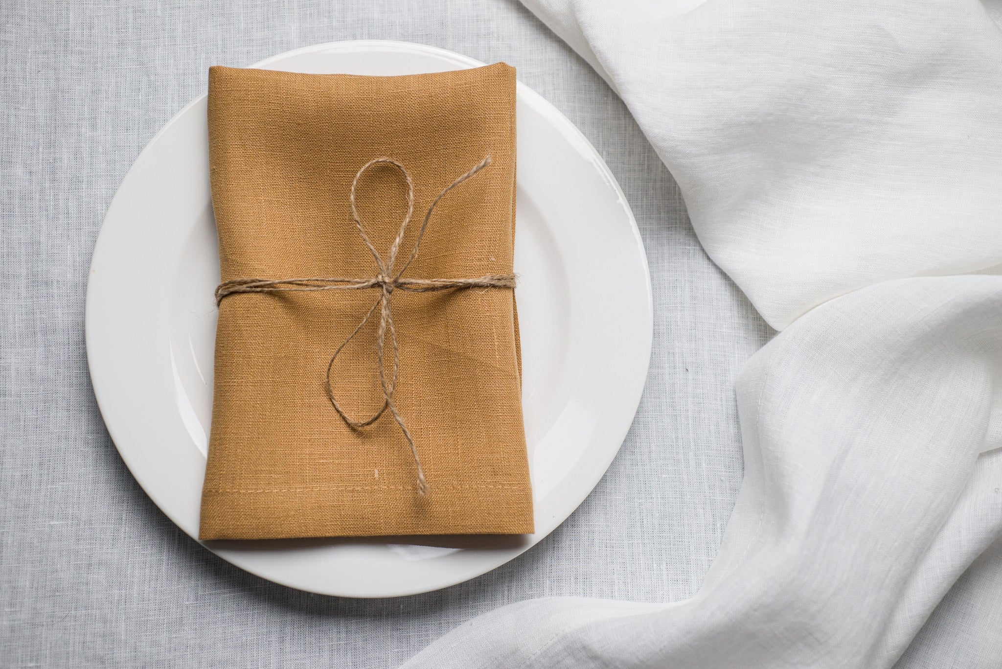 Honey linen napkin tied with jute twine on a white plate