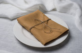 Honey linen napkin tied with jute twine on a white plate, side view