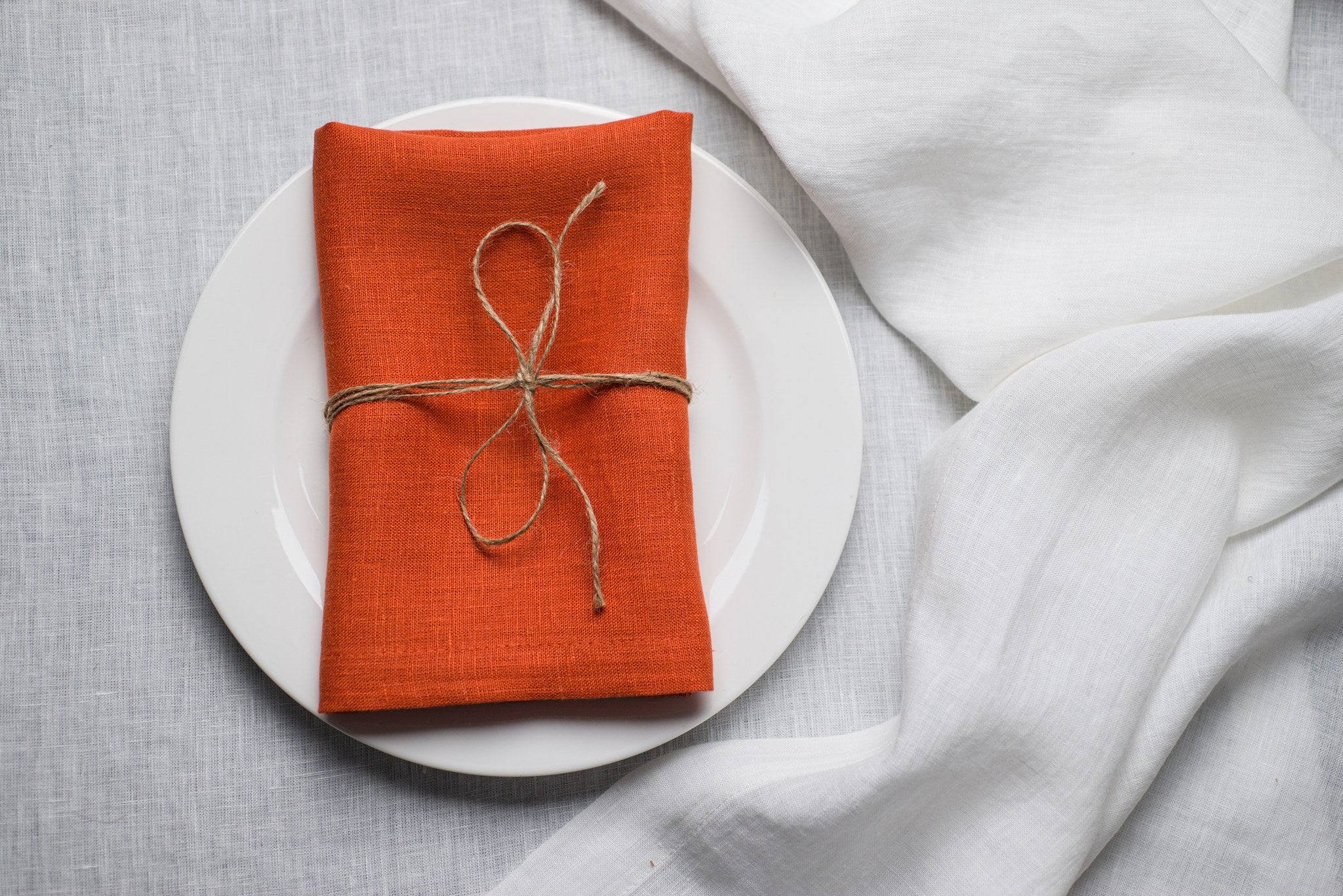 Terracotta linen napkin tied with jute twine on a white plate