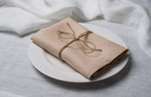 Sand linen napkin tied with jute twine on a white plate, side view