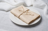 Natural Beige linen napkin tied with jute twine on a white plate, side view