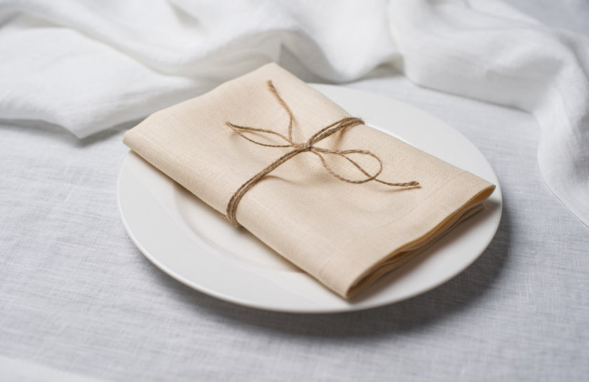 Natural Beige linen napkin tied with jute twine on a white plate, side view