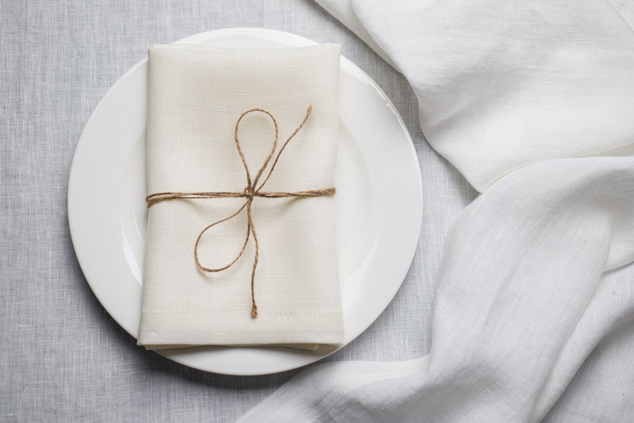 Milk linen napkin tied with jute twine on a white plate