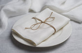 Milk linen napkin tied with jute twine on a white plate, side view