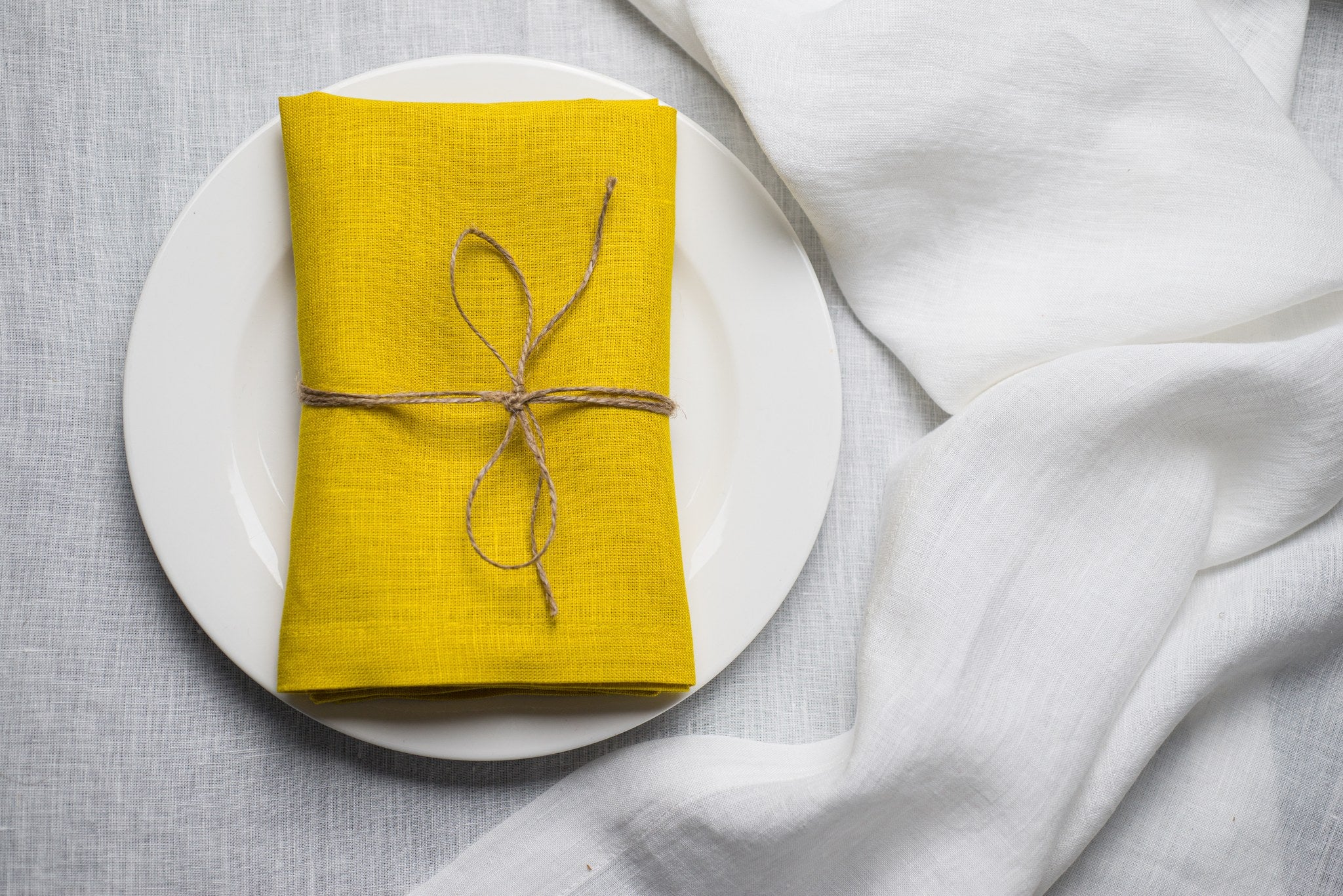 Lemon linen napkin tied with jute twine on a white plate