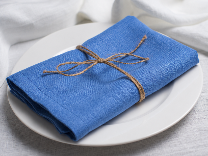 Electric linen napkin tied with jute twine on a white plate, side view