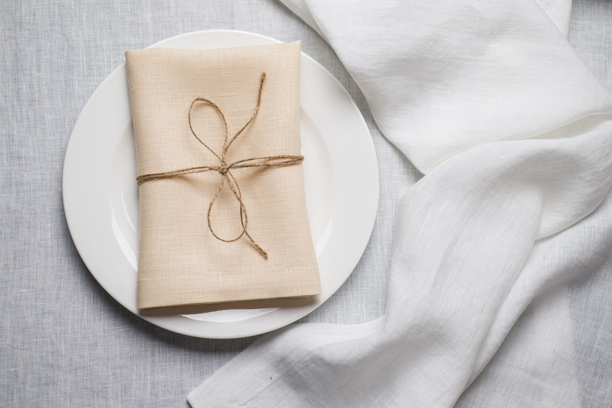 Cream linen napkin tied with jute twine on a white plate