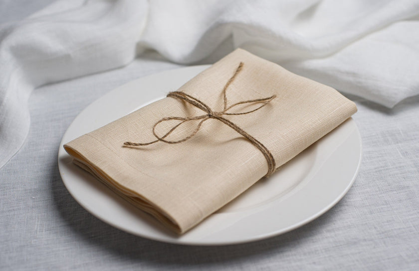 Cream linen napkin tied with jute twine on a white plate, side view