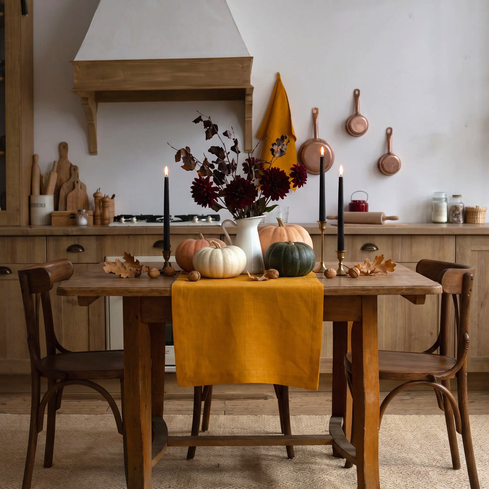 Halloween table setting with a mustard linen table runner, white, orange and green pumpkins, black taper candles and burgundy dahlias in a rustic kitchen – CoolLinen