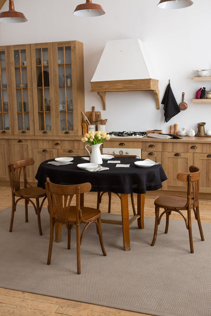Black round linen tablecloth on a wooden dining table in a rustic kitchen