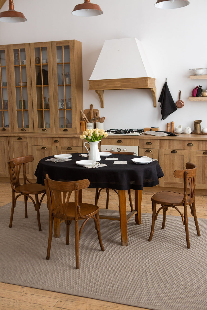 Black round linen tablecloth on a wooden dining table in a rustic kitchen