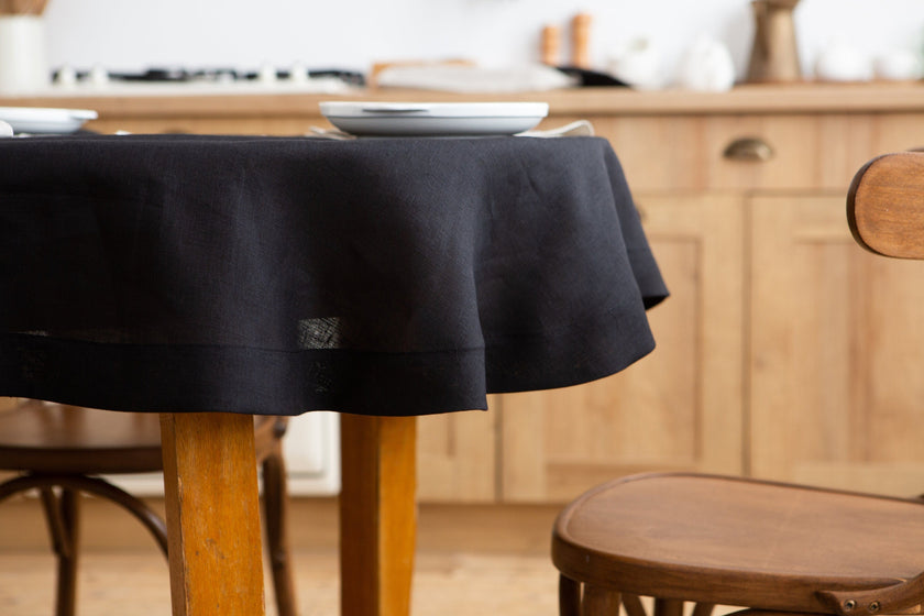 Black round linen tablecloth draped over a dining table, close-up