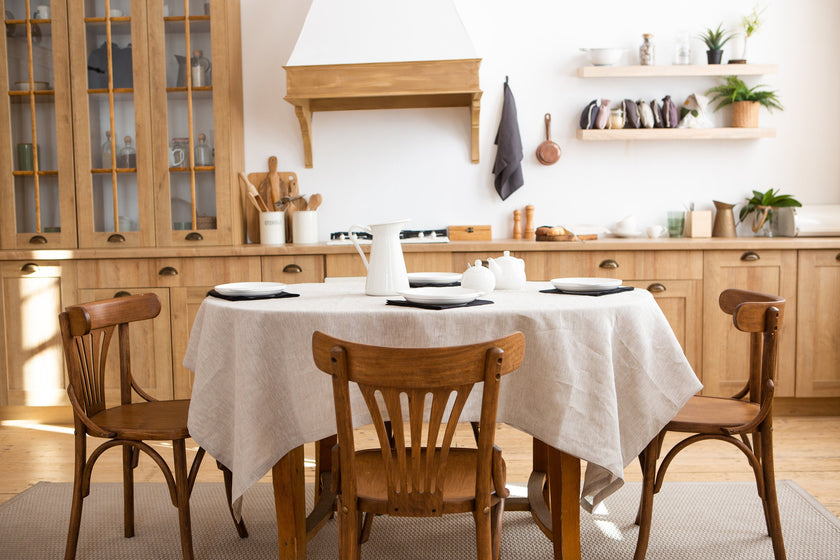 Natural linen tablecloth on a wooden dining table with chairs in a cozy kitchen interior.