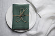 Green basil linen napkin with mitered corners on white plate, natural flax table setting, reusable eco friendly cloth napkin for everyday dining