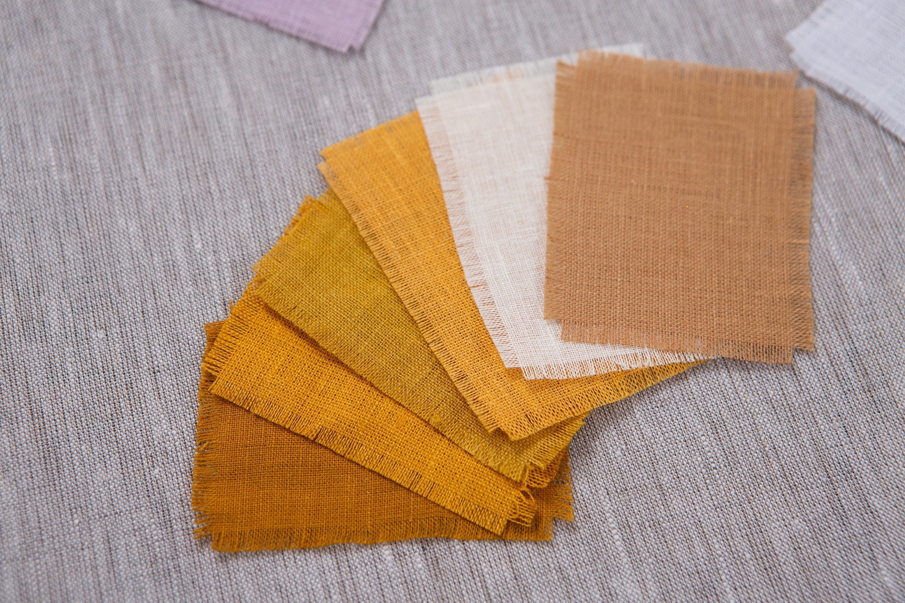 A variety of organic linen fabric samples in a warm yellow-hot mustard palette